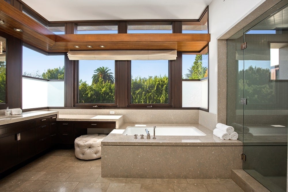 这是一间浴室，里面有一个大浴缸，铺着与地板相同的瓷砖，与梳妆台的深色橱柜和淋浴区的玻璃门形成对比。图片来自Toptenrealestatedeals.com。