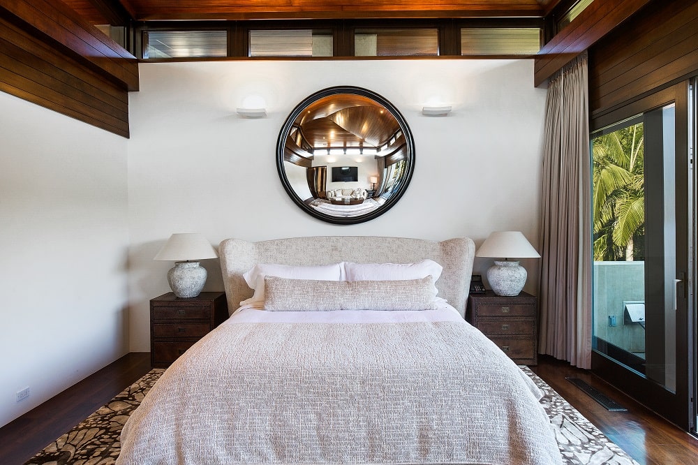 主卧室里有一张米色大床，床头板有软垫，上面有一面巨大的圆形壁挂镜。图片来自Toptenrealestatedeals.com。