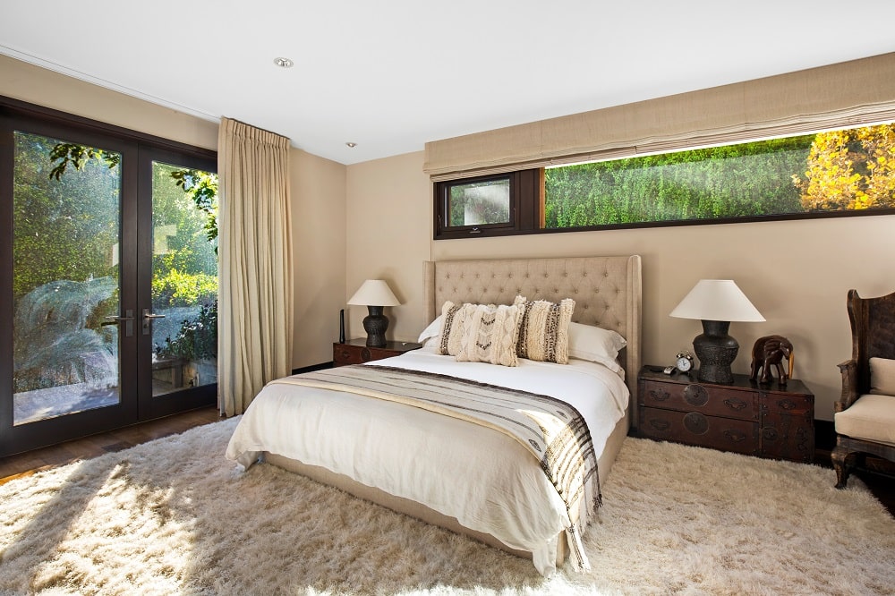 另一间卧室的墙壁是米色的，与米色的簇绒床头板相匹配，两侧是深色的木制床头抽屉和台灯。图片来自Toptenrealestatedeals.com。