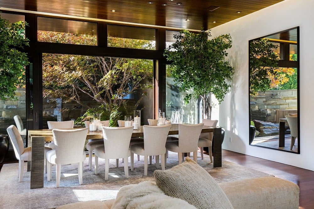 这是一个靠近客厅的用餐区，有一个大的长方形餐桌，周围环绕着白色的椅子，并装饰着一盆大盆栽。图片来自Toptenrealestatedeals.com。