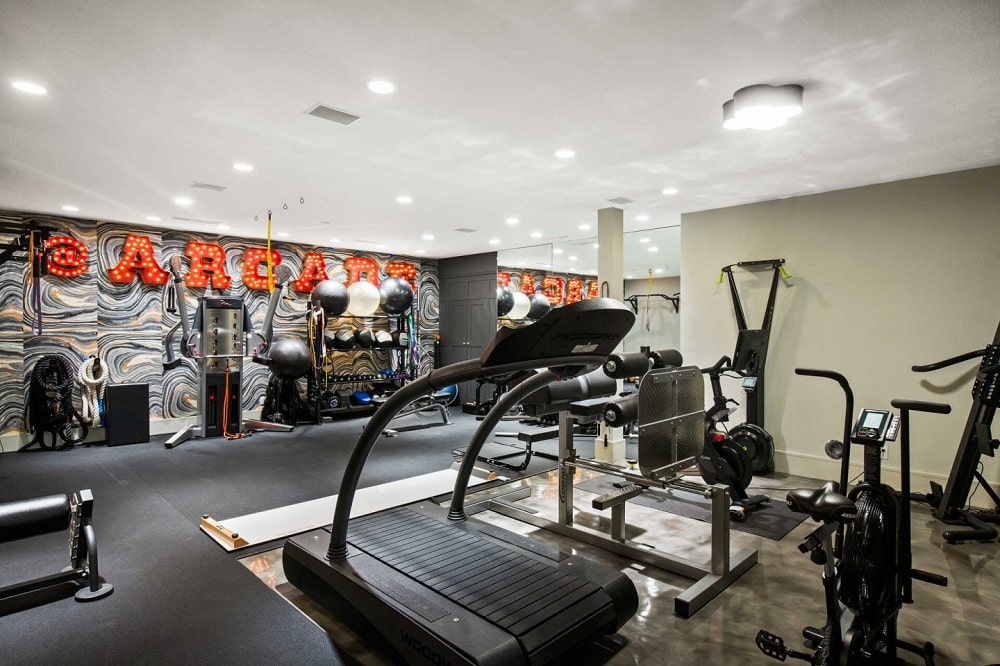这是一个大型的家庭健身房，有完整的机器和设备，以及镜面墙壁和大型墙壁装饰。图片来自Toptenrealestatedeals.com。
