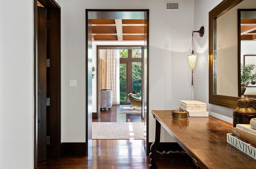 这是房子里的一条走廊，旁边有一张大的木制控制台桌子，上面有一面镜子和壁挂式灯具。图片来自Toptenrealestatedeals.com。