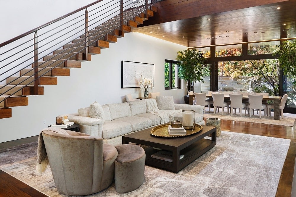 这是一个靠近楼梯一侧的客厅，一个大米色沙发在有图案的地毯上，与深色的木制咖啡桌形成对比。图片来自Toptenrealestatedeals.com。