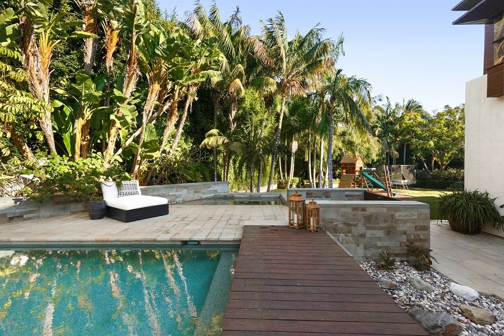 泳池一侧有一条木制走道，通向泳池旁的休息区，周围是郁郁葱葱的热带树木。图片来自Toptenrealestatedeals.com。