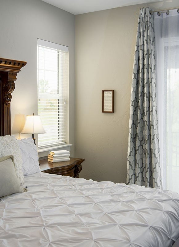 主卧室有米黄色的墙壁和一张舒适的木床，上面盖着豪华的白色被子。