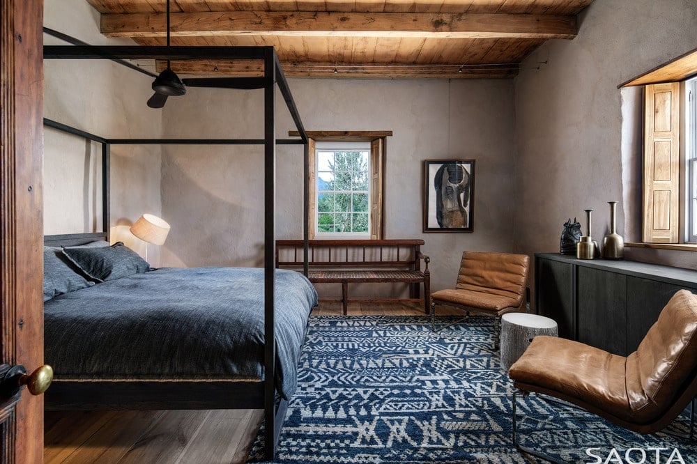 主卧室有一张大的深色木制四柱床，辅以有图案的区域地毯和上面的木制横梁天花板。