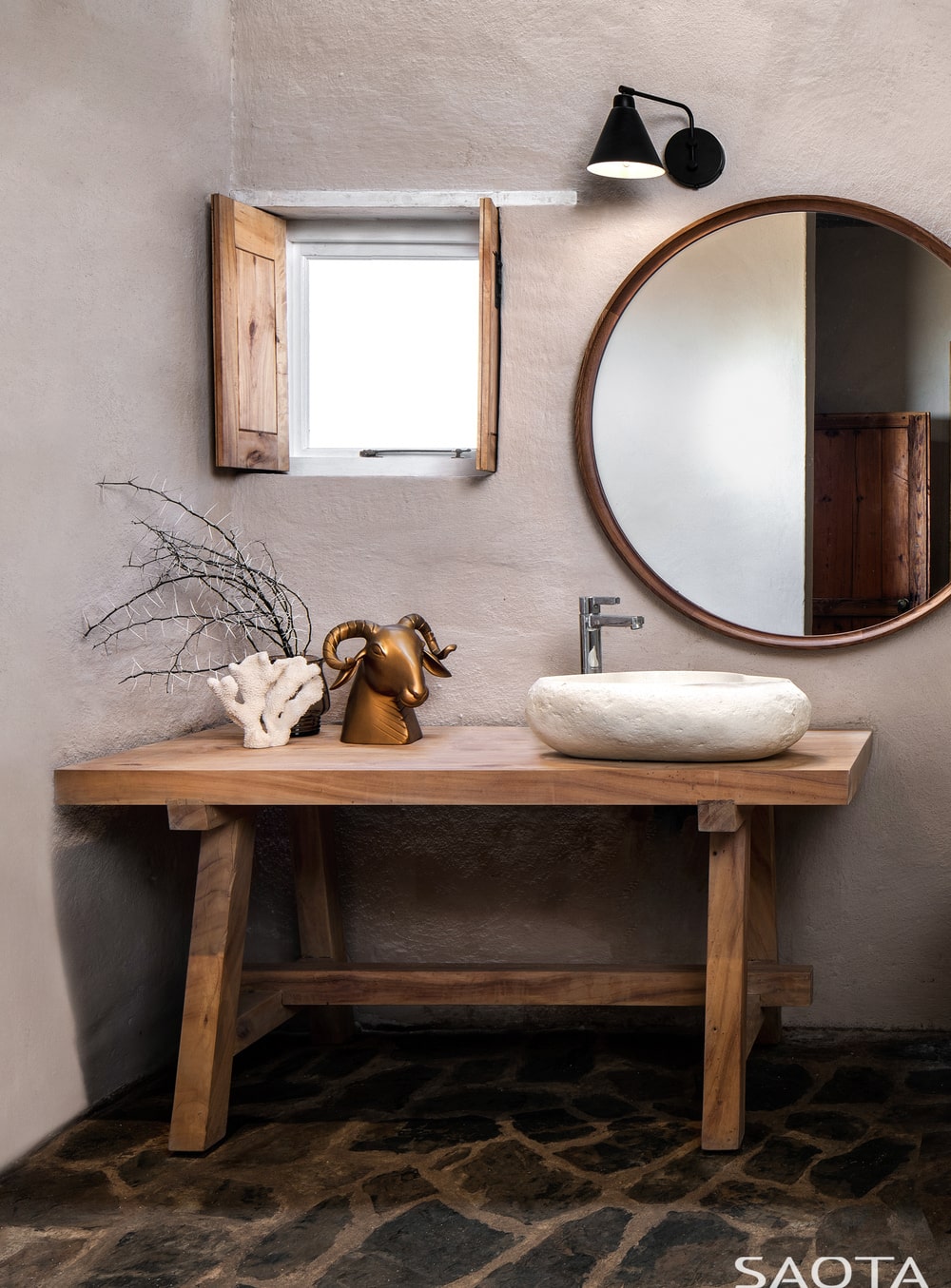 这是一个乡村浴室的近距离观察，有一个木桌作为梳妆台来支撑水槽，配上一个小窗户和一面大镜子。