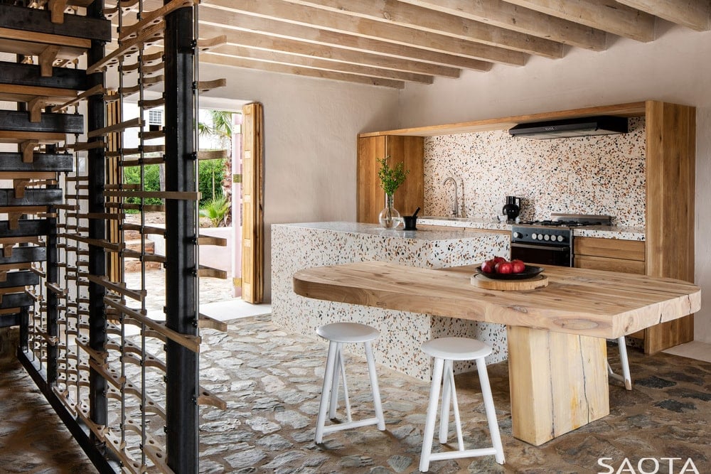 这是另一个大的木制餐桌，它附着在厨房岛上，与白色的凳子搭配在厨房的框架上。