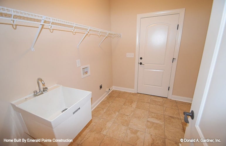 洗衣房与石灰石地板，白色金属挂钩，和一个公用水槽。