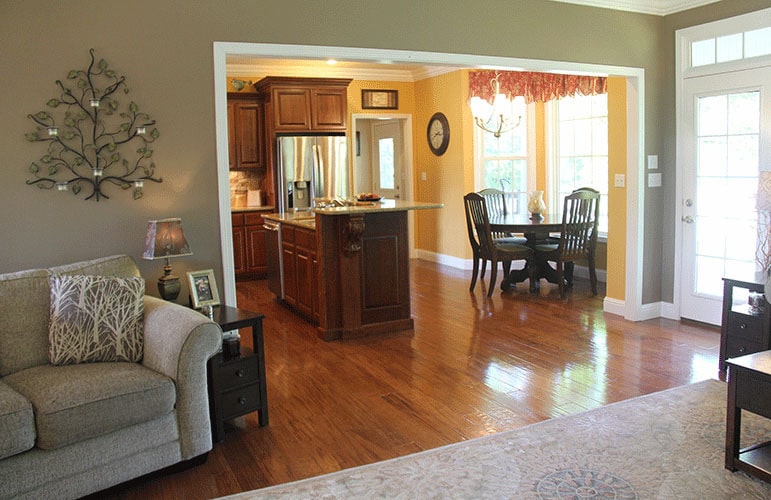 客厅有天然硬木地板，灰褐色的墙壁，一个超大的开口通往厨房和早餐角。
