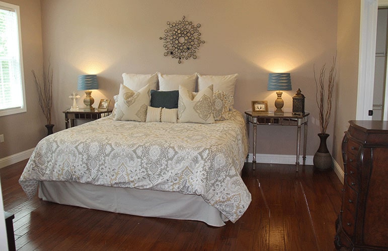主卧室有装饰性的墙壁艺术和一张舒适的床，两侧有镜子床头柜。