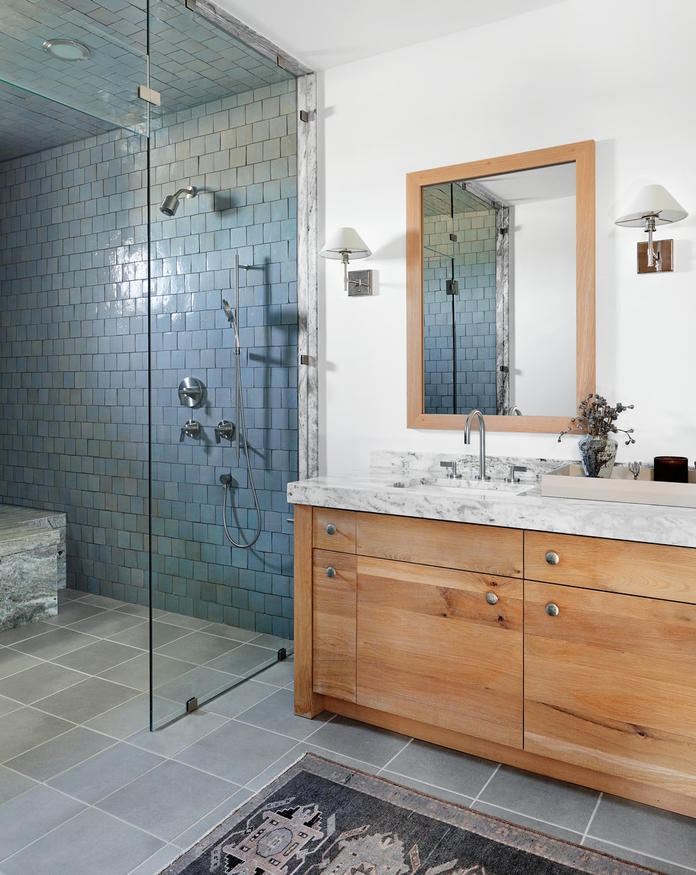 这是一个简单的浴室，有一个木制梳妆台，上面有一面配套的镜子，旁边是镶有深色瓷砖的玻璃淋浴区。
