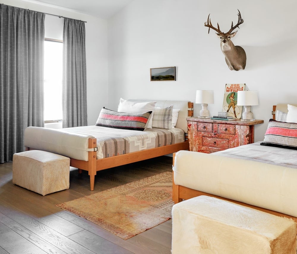 这间卧室有两张床的空间，床上有简单的木框，与中间的木制梳妆台相匹配，梳妆台顶部有一个壁挂式的狩猎奖杯。