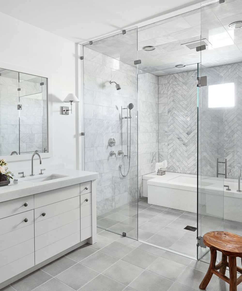 这是一间明亮的浴室，有一个白色的梳妆台，远处的墙上有一个玻璃围成的淋浴和浴缸的湿区。