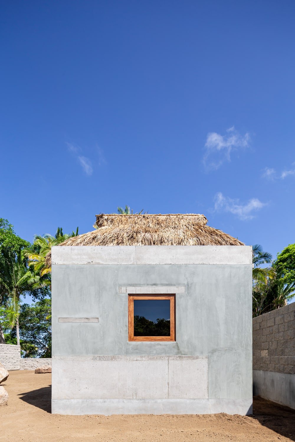 这是房子的立面，展示了混凝土外墙和棕榈屋顶。