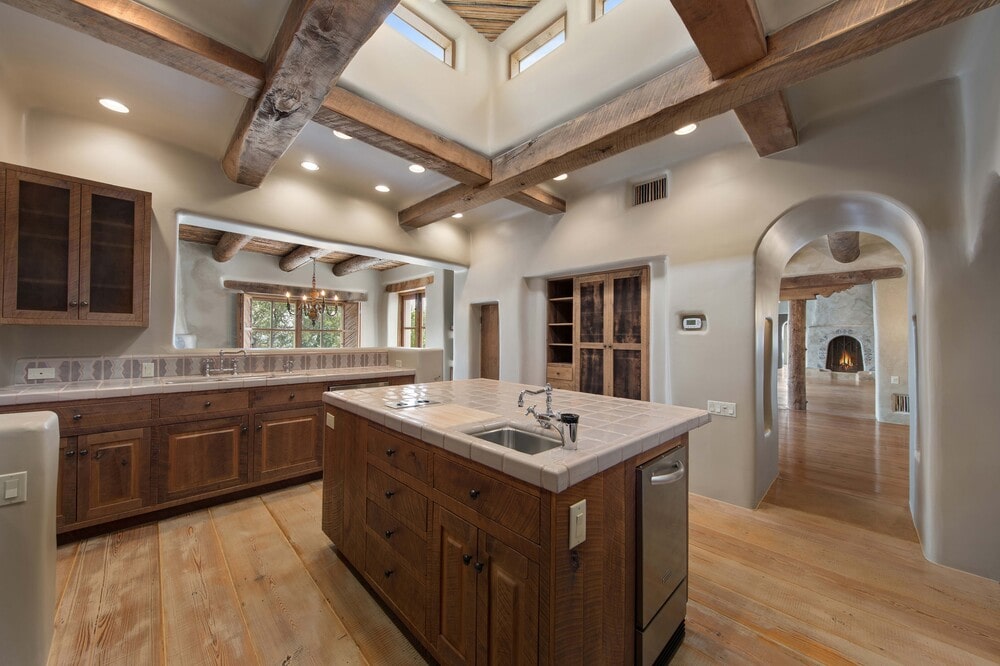 这是一间厨房，中间有一个很大的厨房岛台，棕色的木制橱柜与墙壁上的橱柜和天花板上裸露的横梁相匹配。图片来自Toptenrealestatedeals.com。