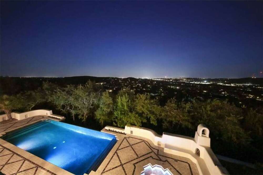 这是阳台的夜景，展示了游泳池的空灵光芒，以及高大树木之外的城市灯光。图片来自Toptenrealestatedeals.com。
