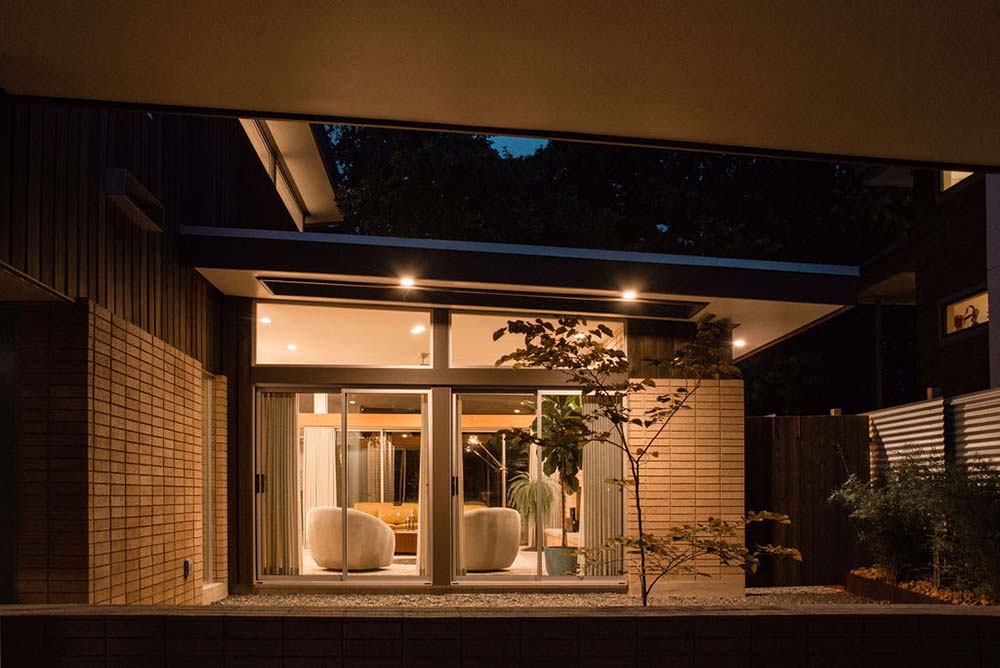 这是夜晚的房屋景观，展示了温暖的照明，并通过玻璃门瞥见室内。