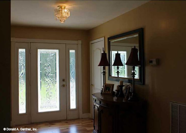 门厅里有一扇玻璃门和一张木制的控制台桌子，上面有一面镜框镜子。