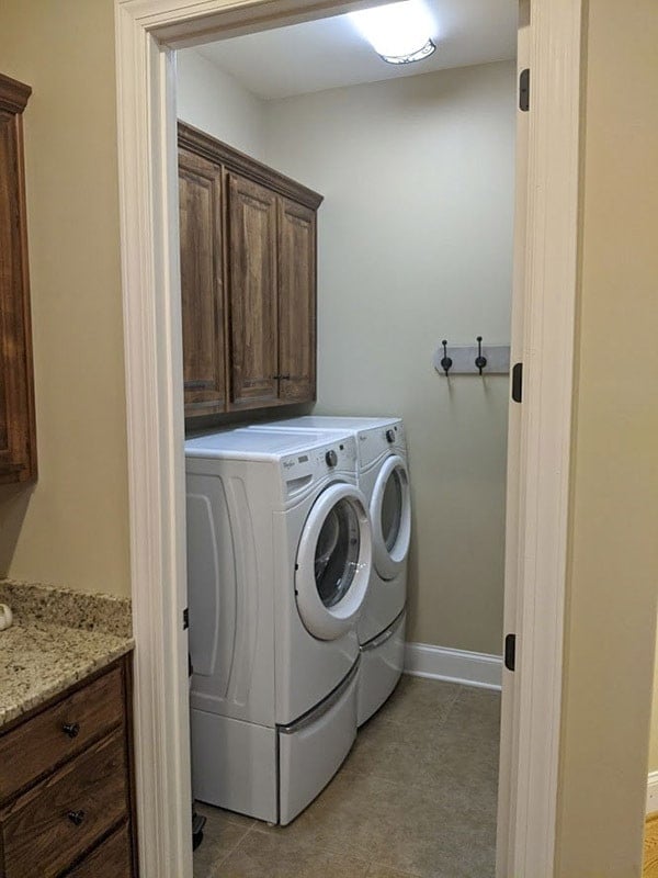 较小的洗衣房，配有白色前置电器和悬垂橱柜。