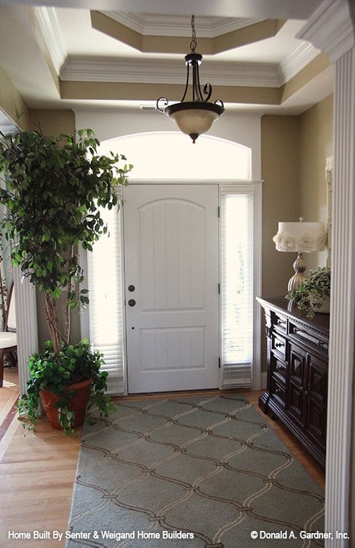 门厅里有一张深色的木桌，一块有图案的区域地毯，白色的前门周围有侧灯和拱形横梁。