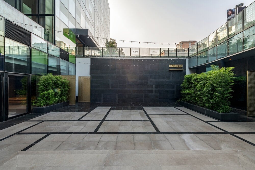 下面一层是办公大楼的大入口，装饰着灌木和深色瓷砖，与浅米色瓷砖和玻璃形成鲜明对比。