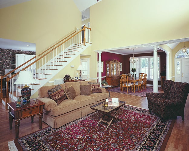 客厅设有带裙边的组合家具和带图案的翼背椅，椅子放在经典的区域地毯上。