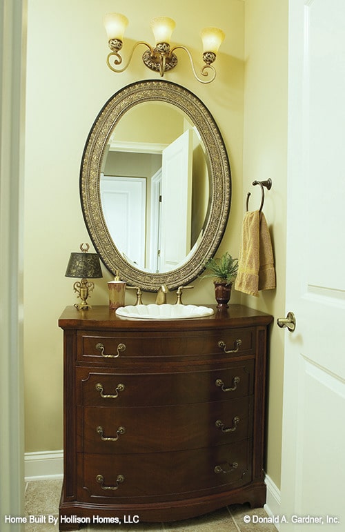 化妆室有一个深色的木质梳妆台，配有一面装饰性的椭圆形镜子。