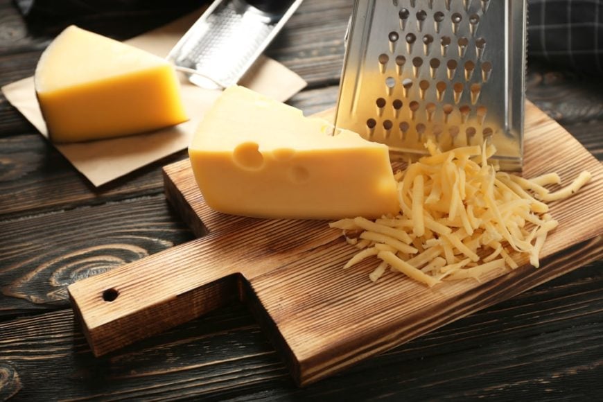 在切菜板上用奶酪刨丝器把奶酪片切碎。