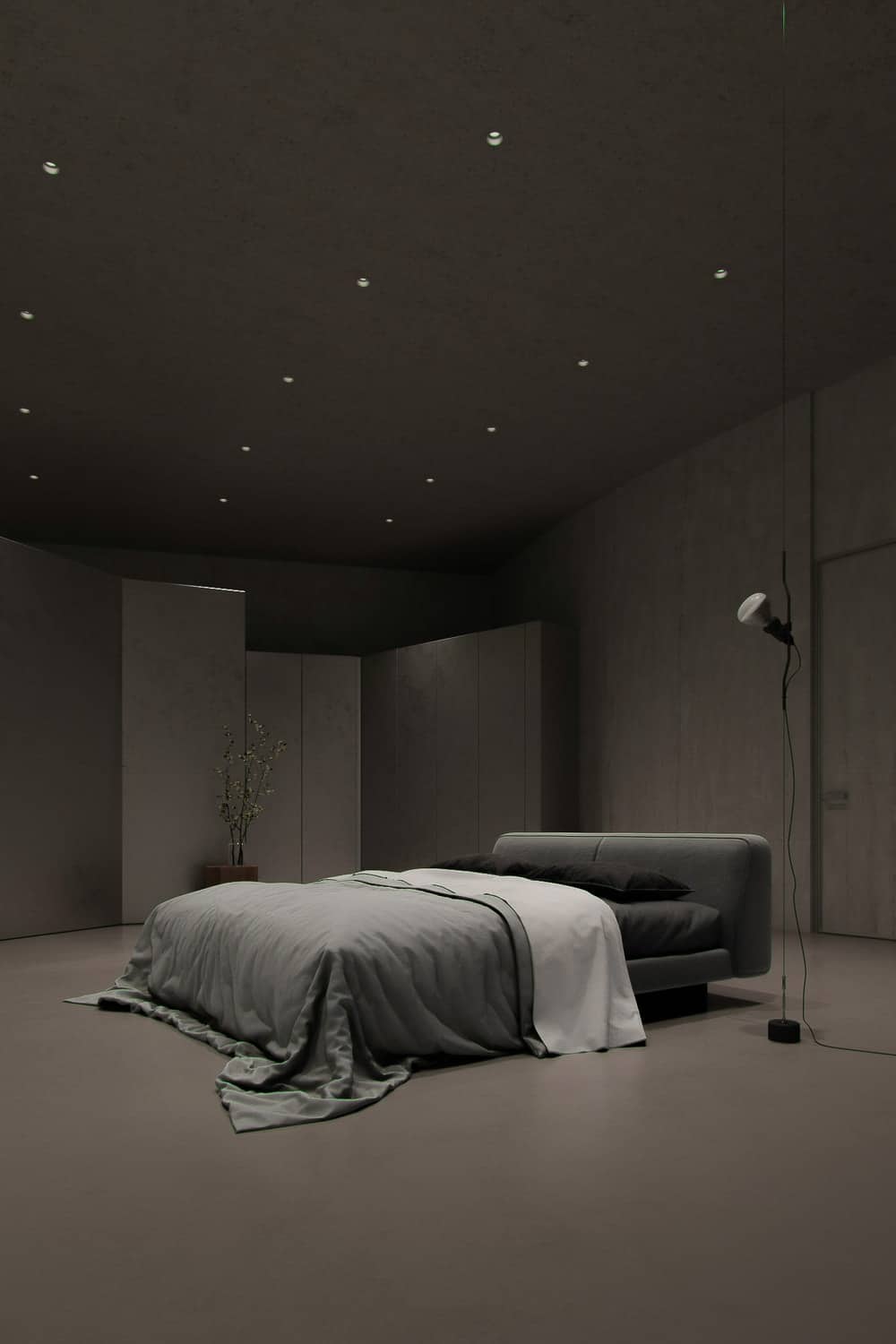 这间卧室里有一张灰色的软垫床，中间是灰色的混凝土墙、地板和天花板，天花板上有嵌壁灯。