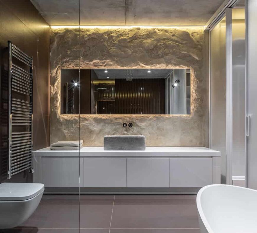 这是主浴室的外观，灰色地砖与另一侧的白色梳妆台、白色马桶和白色独立式浴缸形成对比。