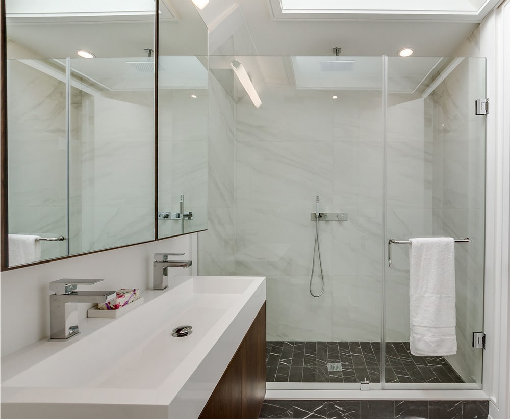 浴室的另一侧有一个玻璃围成的淋浴区，地板上铺着深色瓷砖，墙上贴着白色大理石瓷砖。