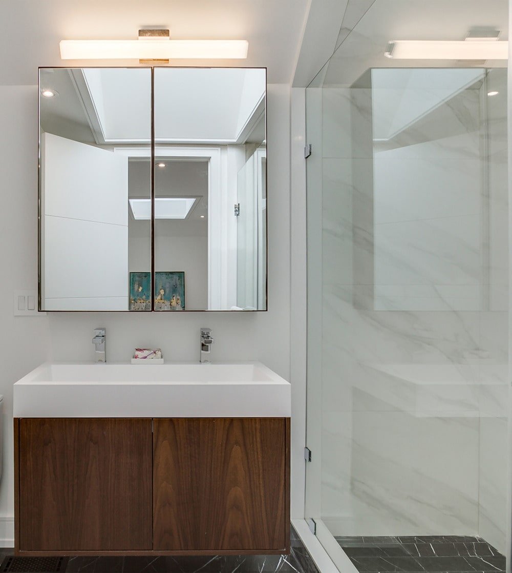 在淋浴区的一侧是梳妆台，它有一个白色的水槽和柜台，与下面的深色木柜和上面的镜子形成对比。