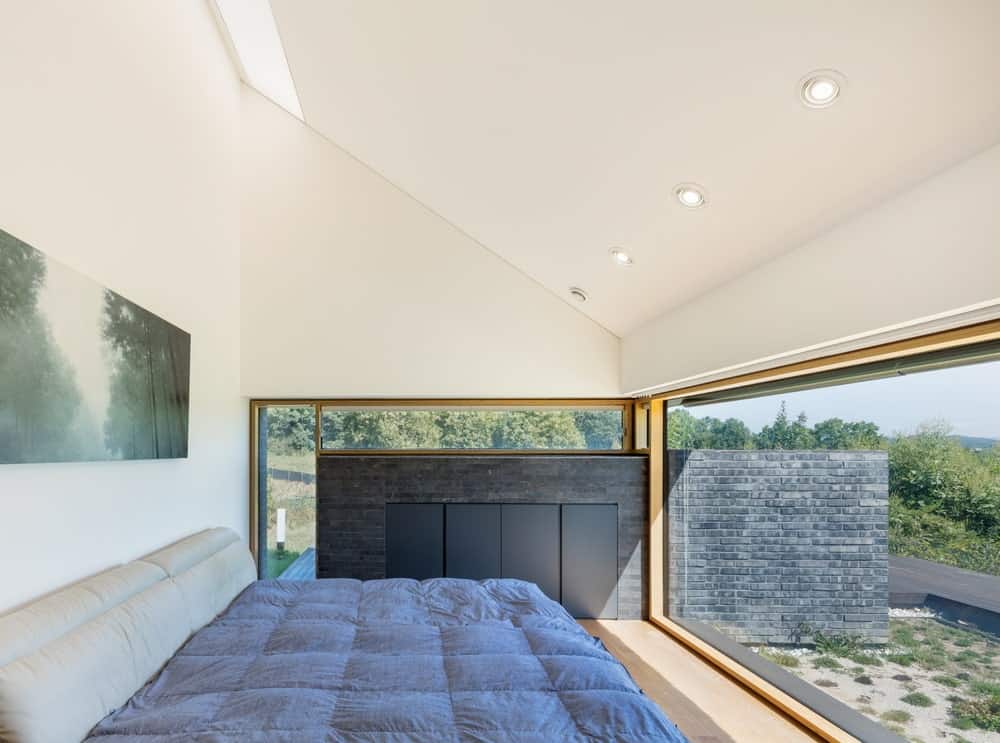 这是一间有玻璃墙和明亮的白色拱形天花板的卧室，上面是硬木地板上的平台床。