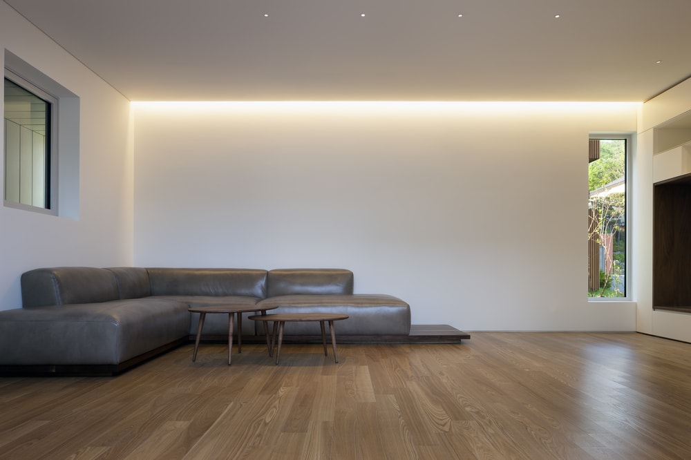 这是一个简单的极简主义客厅，以大型灰色皮革组合沙发为主，辅以两张与硬木地板相匹配的木制咖啡桌。
