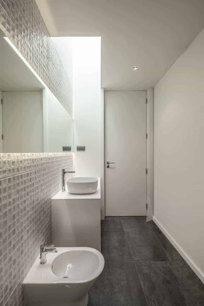 浴室里铺着深灰色的地砖，与明亮的米黄色墙壁、瓷砖和水池的结构形成对比，水池顶部有一面延伸到两侧的明亮镜子。