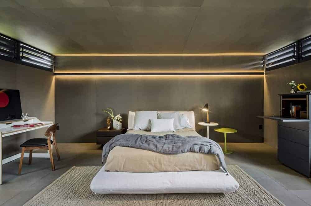 这是主卧室的外观，混凝土墙壁、地板和天花板由白色床上方的现代照明装饰，两侧是各种床头柜。