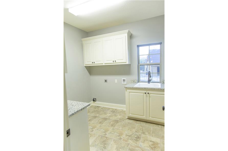 洗衣房有白色橱柜，花岗岩台面，窗户下有一个瓷水槽。