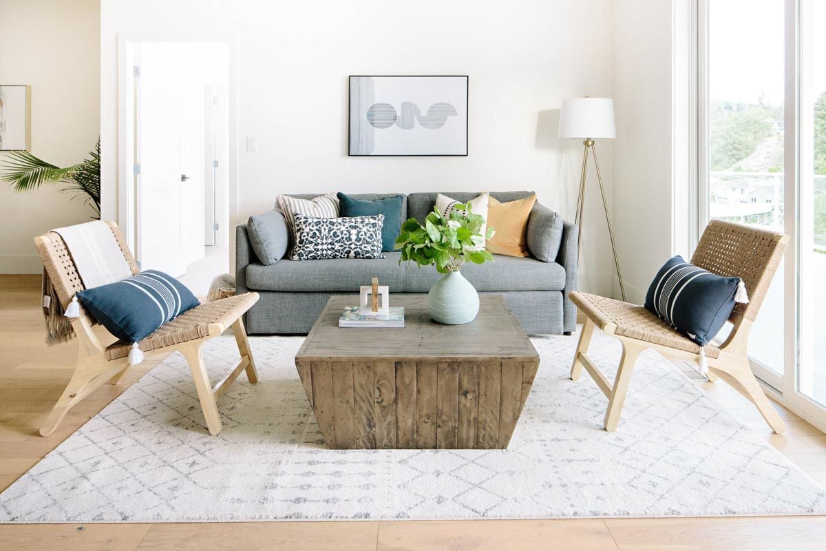 起居室和一个灰色的沙发,柳条椅子,和一个乡村的咖啡桌,坐在一个有图案的面积地毯。