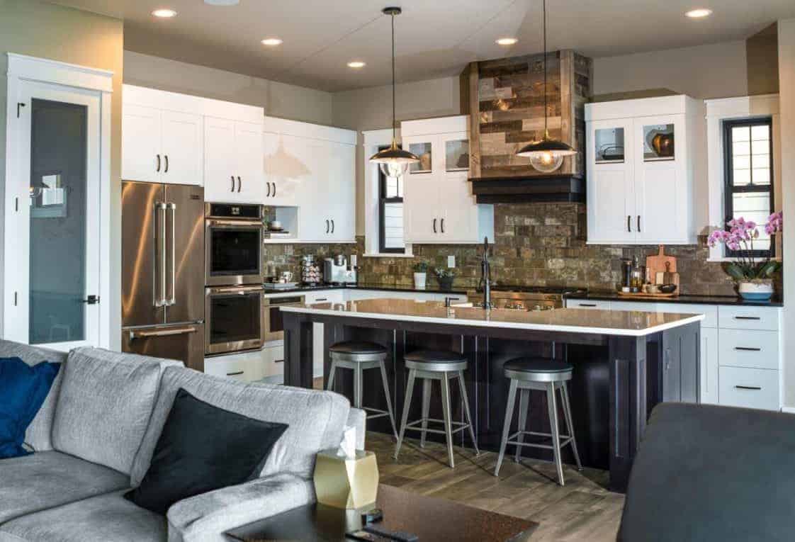 这间厨房里有白色的橱柜和不锈钢电器，与后挡板和通风罩的棕色木制色调形成鲜明对比，后者具有乡村美学。