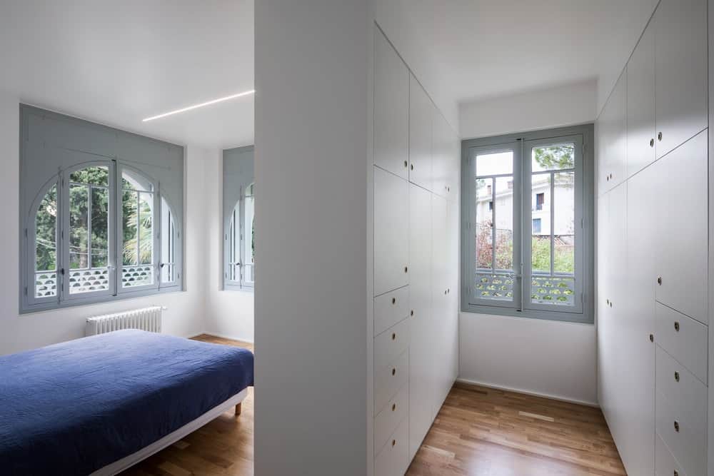 这是一间极简主义风格的卧室，有一张简单的平台床，硬木地板，白色墙壁和带有嵌入式橱柜的白色分隔结构。
