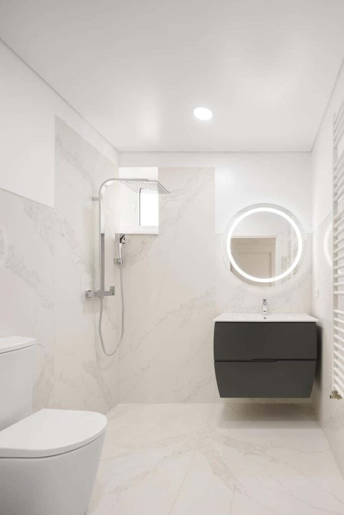 这是一个极简主义的浴室，地板和墙壁上都有一致的亮米黄色大理石。这使得黑色漂浮的梳妆台突出，上面有一个圆形的梳妆台镜子。
