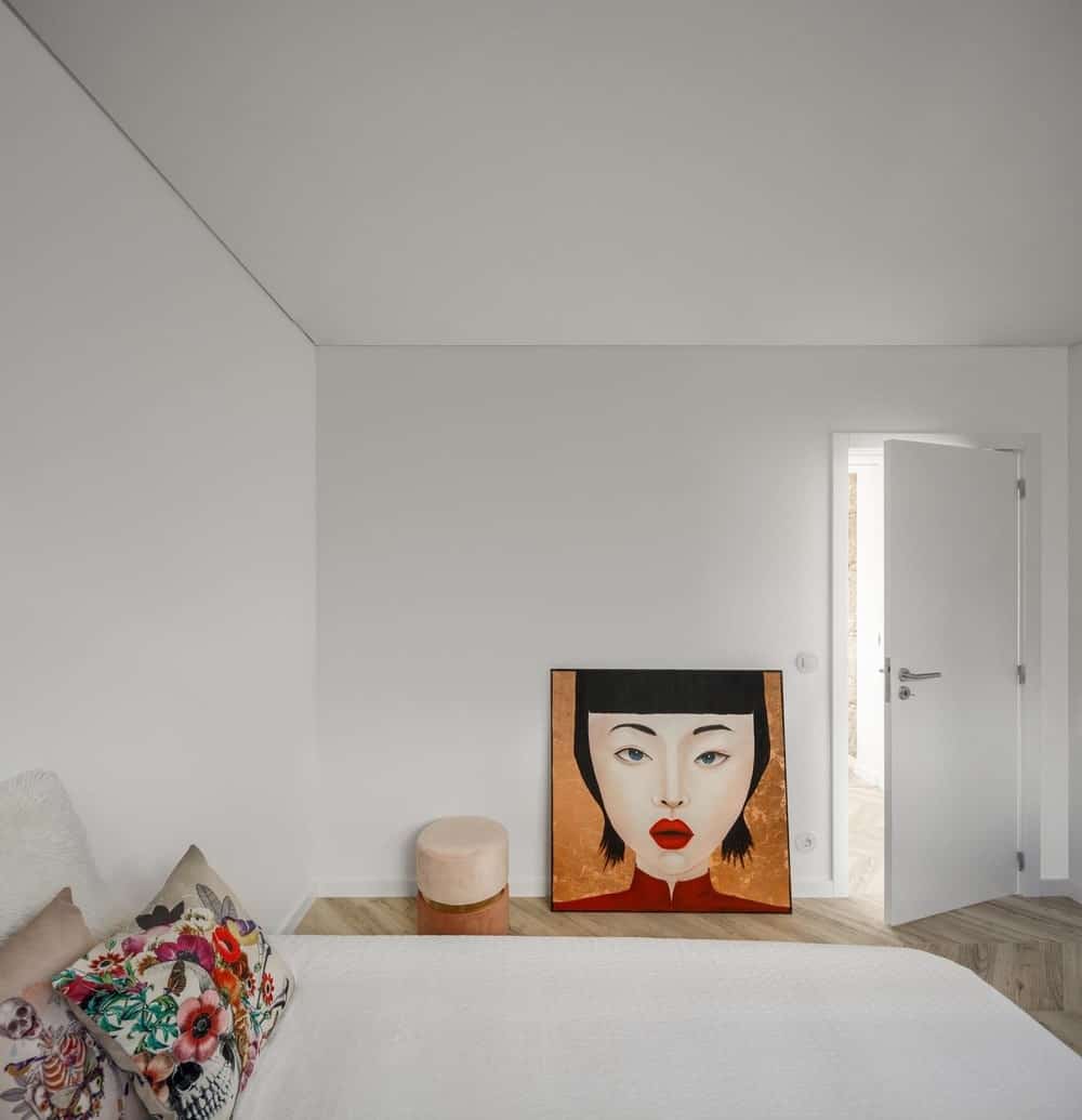 这是一间简单的卧室，白色的床与白色的墙壁和天花板相匹配。然后，墙上的艺术品和枕头作为补充。