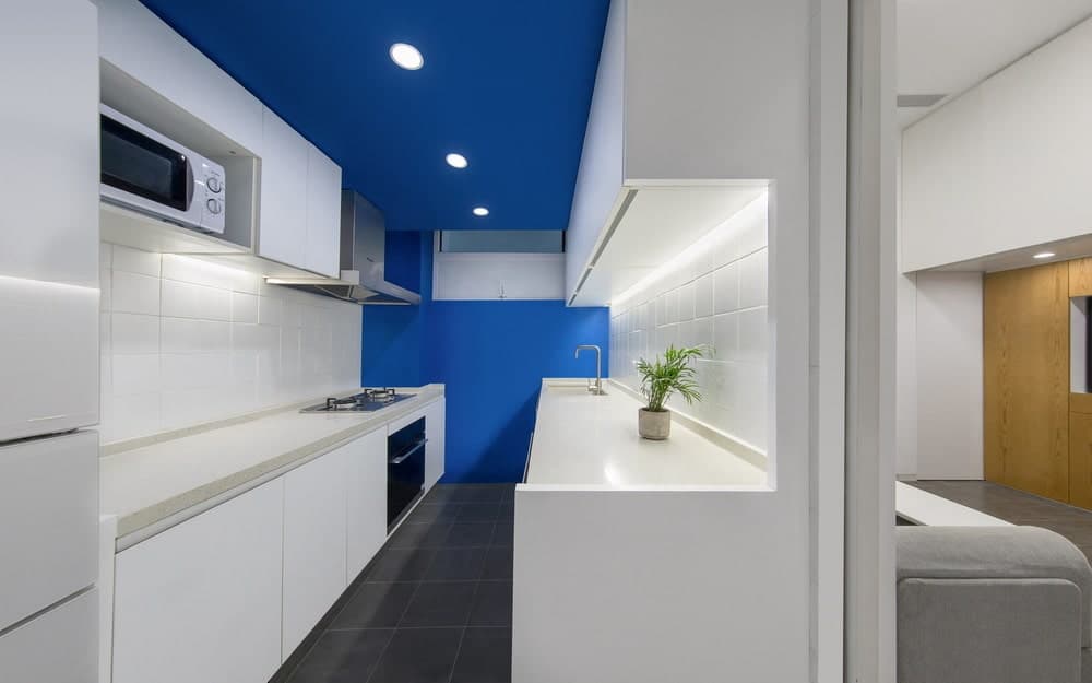 这是一个近距离看看长而狭窄的简约现代厨房，双方都有白色橱柜，由天花板和远壁的蓝色宽敞。