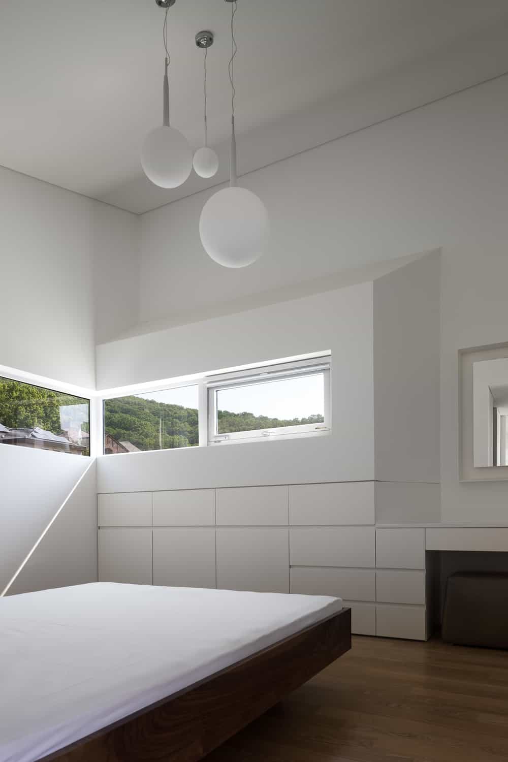 这是一个简单的极简主义卧室，白色的墙壁上有现代的嵌入式抽屉和橱柜，与白色的天花板、白色的吊灯和白色的床相配。这些都是由硬木地板补充。