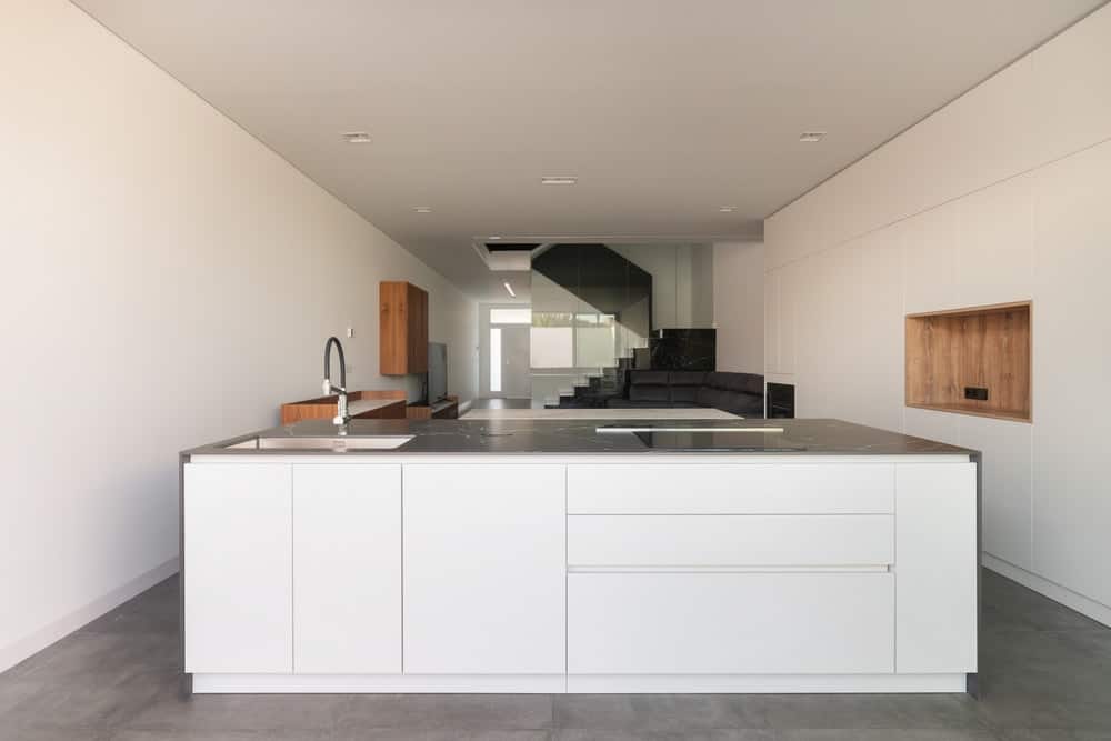 这是一个近距离看看最小的厨房，有一个大型的白色现代厨房岛，与内置的白色橱柜衬砌衬砌的内置白色橱柜。