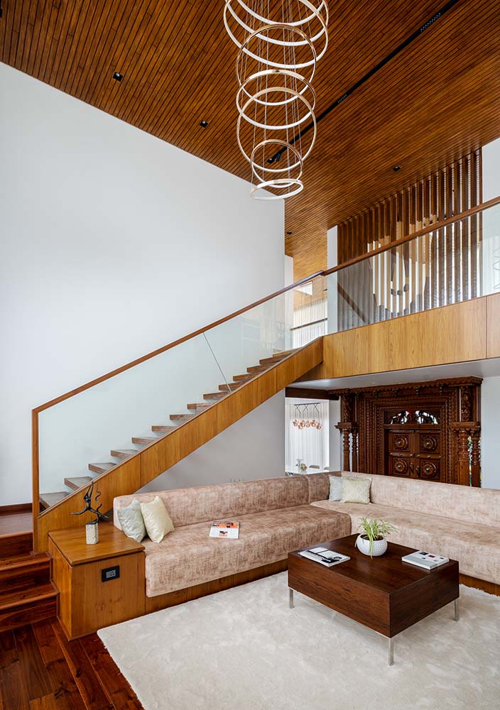 大的l型沙发有一个木制结构，被嵌入楼梯的结构中，上面有米色的靠垫，并搭配一个木制的咖啡桌。