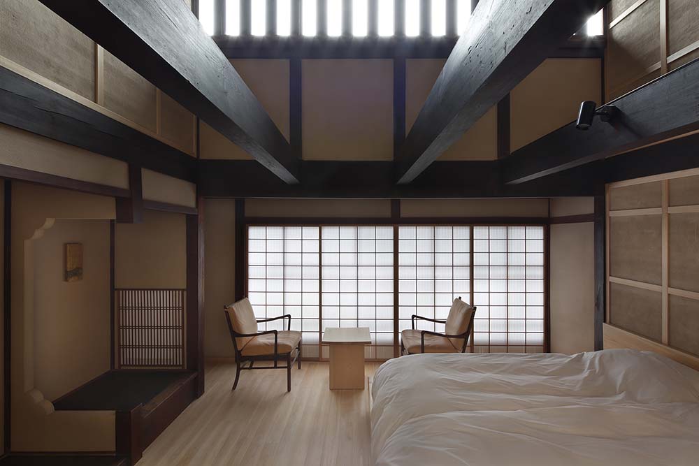 这是另一间卧室的近景，里面有一张大床，上面有裸露的横梁，还有一个靠窗的休息区。