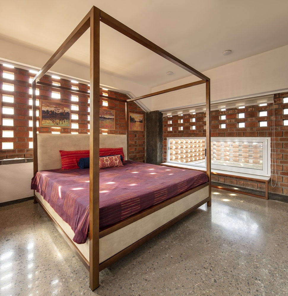 主卧室里有一张大的木制四柱床，与土色的砖面板搭配得很好，板条可以让自然光进来。
