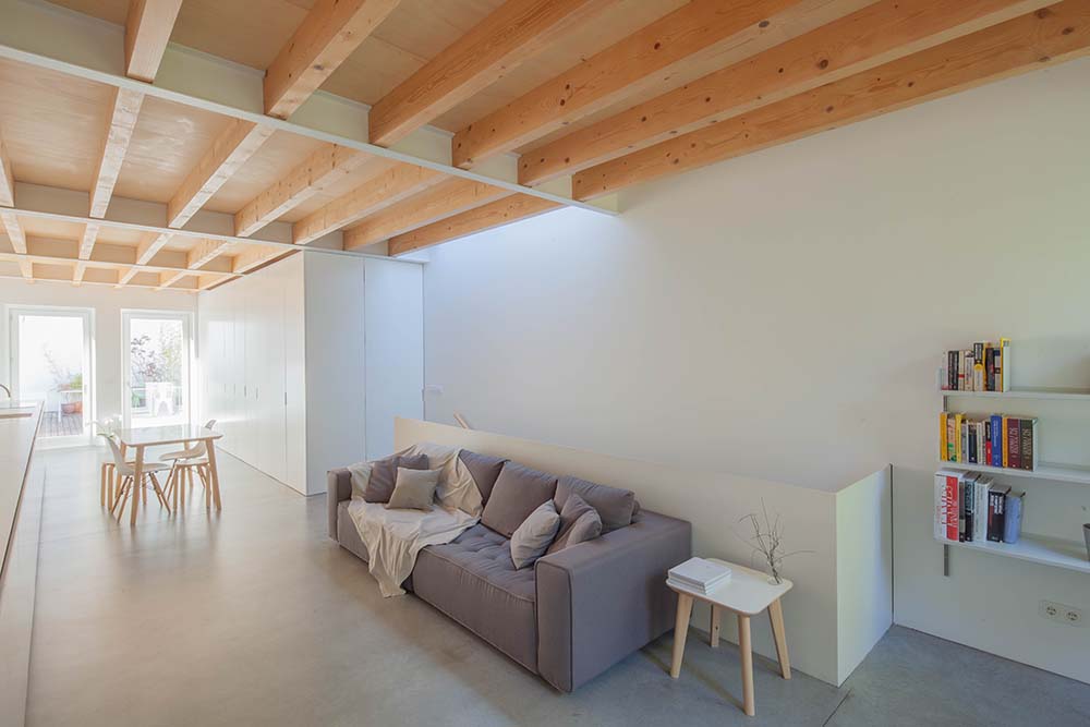 这是极简主义风格的客厅的全貌，里面有一张简单的灰色沙发，搭配着带有内置结构的白墙，上面的木天花板有外露的横梁。